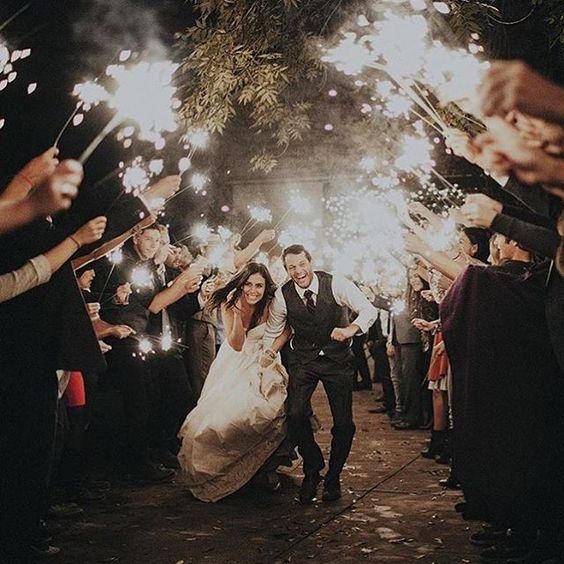 a bride and groom walk through sparklers as they exit their wedding ceremony at night