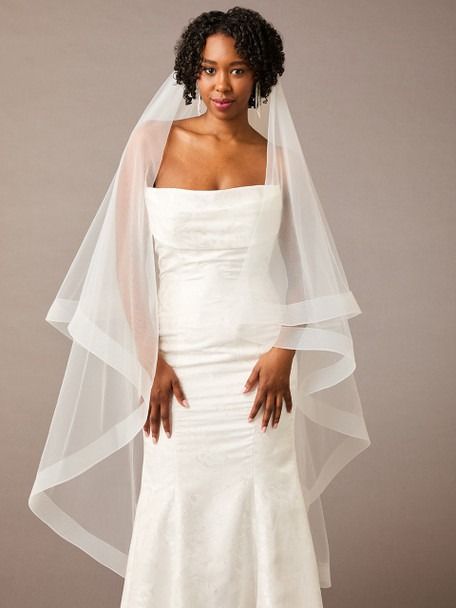 a woman in a white wedding dress with a veil over her head and hands on her hips