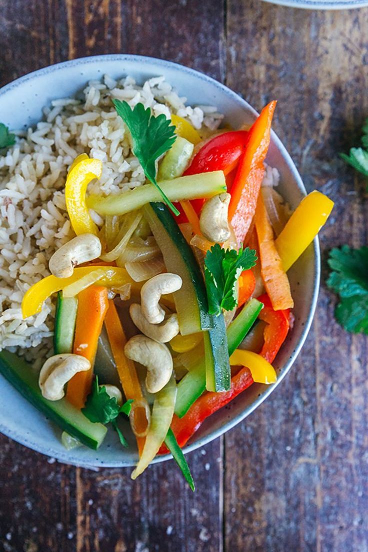 a bowl filled with rice and vegetables on top of a wooden table next to cilantro