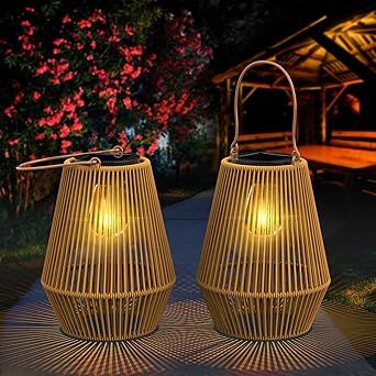 two yellow lanterns sitting on top of a sidewalk next to trees and flowers at night