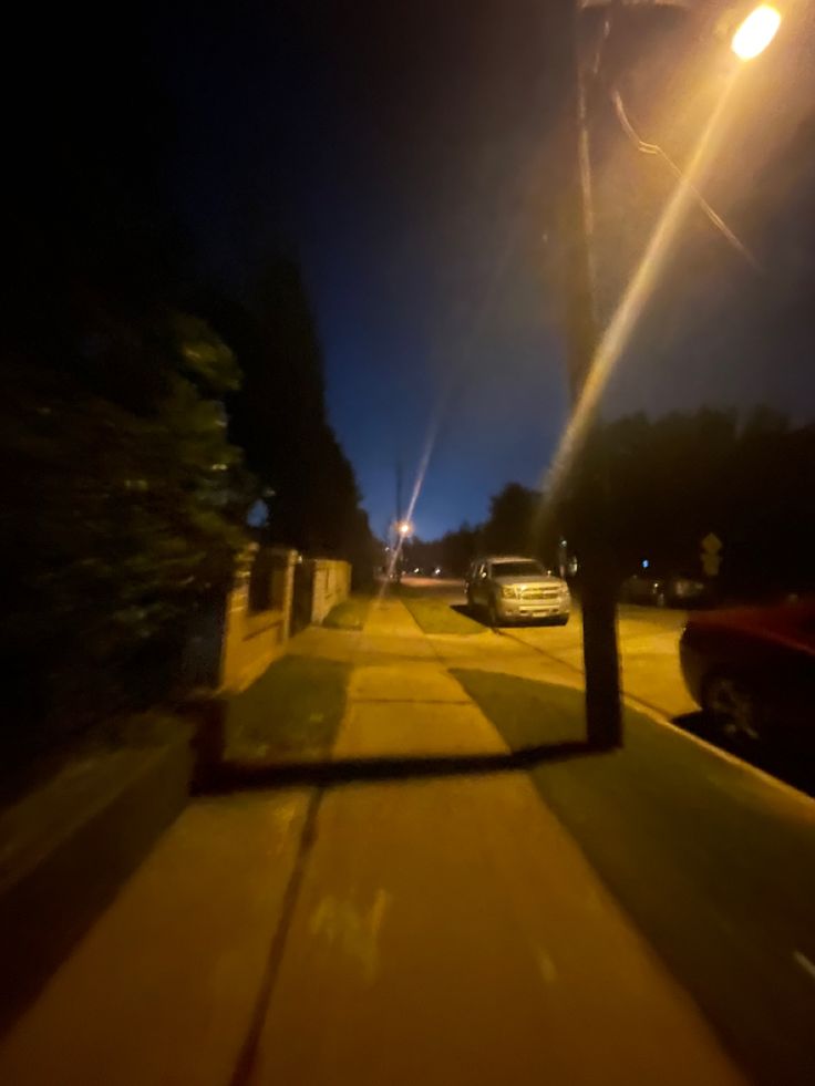 a street at night with cars parked on the side of the road and one car driving down it