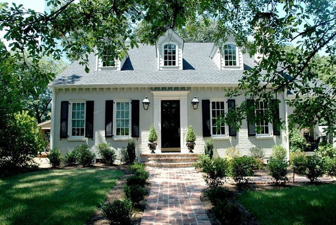 a white house with black shutters on the front door and windows, surrounded by green grass