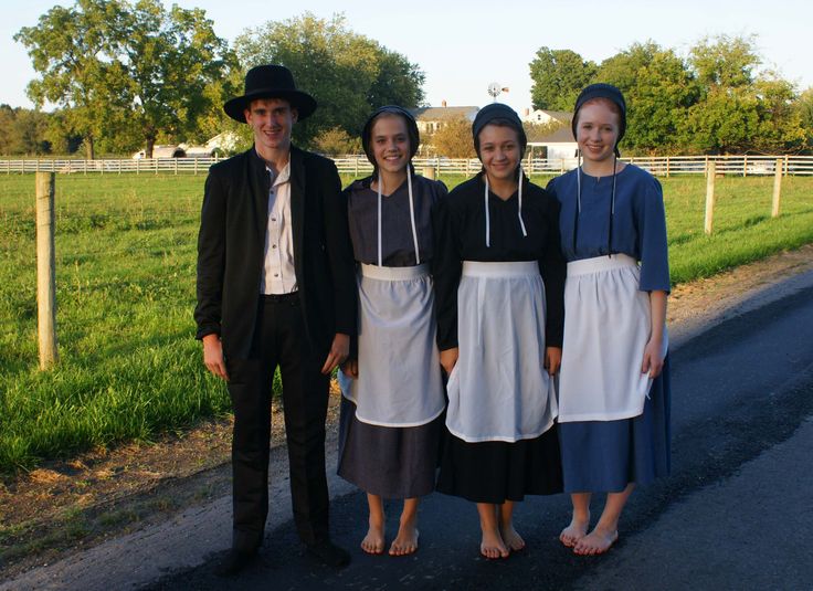 four people standing next to each other in front of a fence and grass covered field