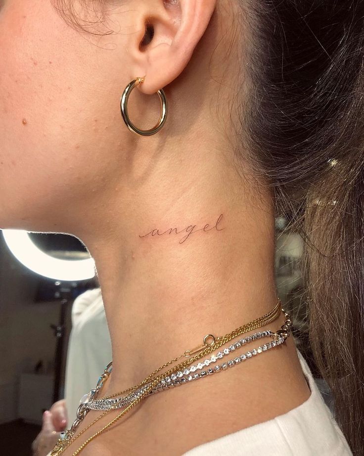 a woman's neck with the word angel tattooed on her left side ribcage