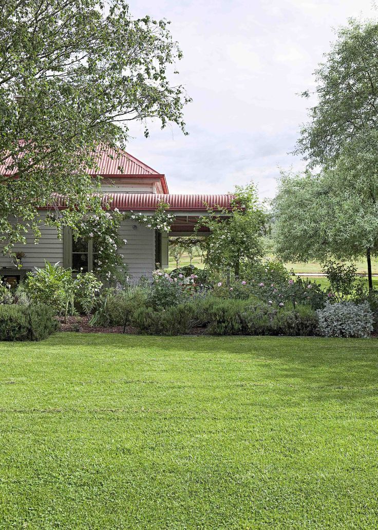 the house is surrounded by lush green grass and trees, with an old - fashioned red tin roof