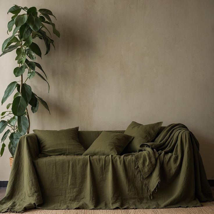 a couch covered in green linen next to a potted plant