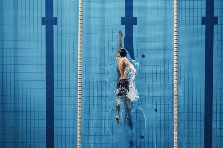 a man is swimming in the pool with his back turned to the camera and he has no shirt on