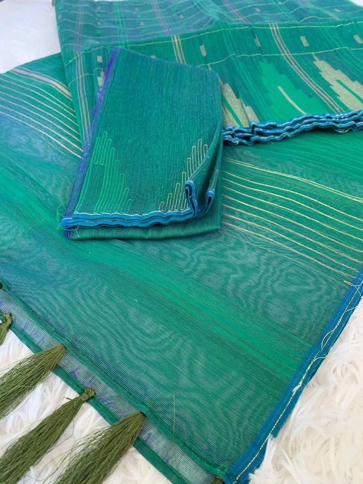 three pieces of green and blue cloth on a white surface with fringes around it