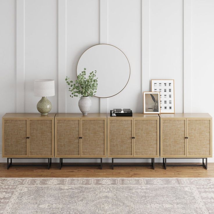 a room with white walls and a large round mirror on the sideboard next to a plant