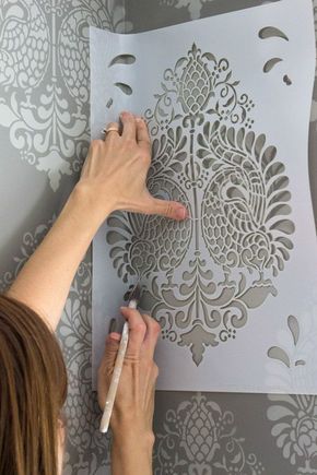 a woman is using a marker to draw on a paper with an intricate pattern in the background