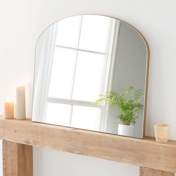 a mirror sitting on top of a wooden mantle next to a potted plant and candles