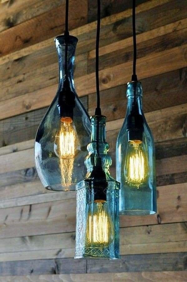 three glass bottles are hanging from the ceiling with light bulbs attached to them, in front of a wooden wall