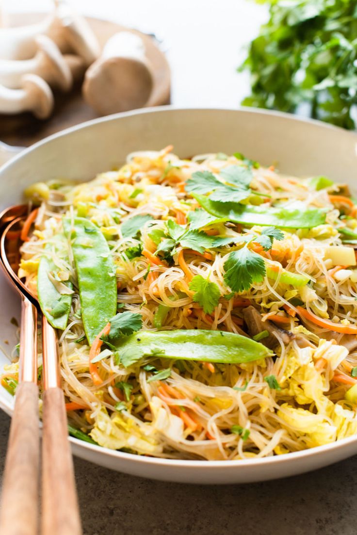 a white bowl filled with food next to chopsticks and garlic on a table