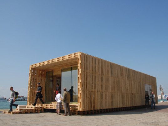 two people walking past a building made out of straw