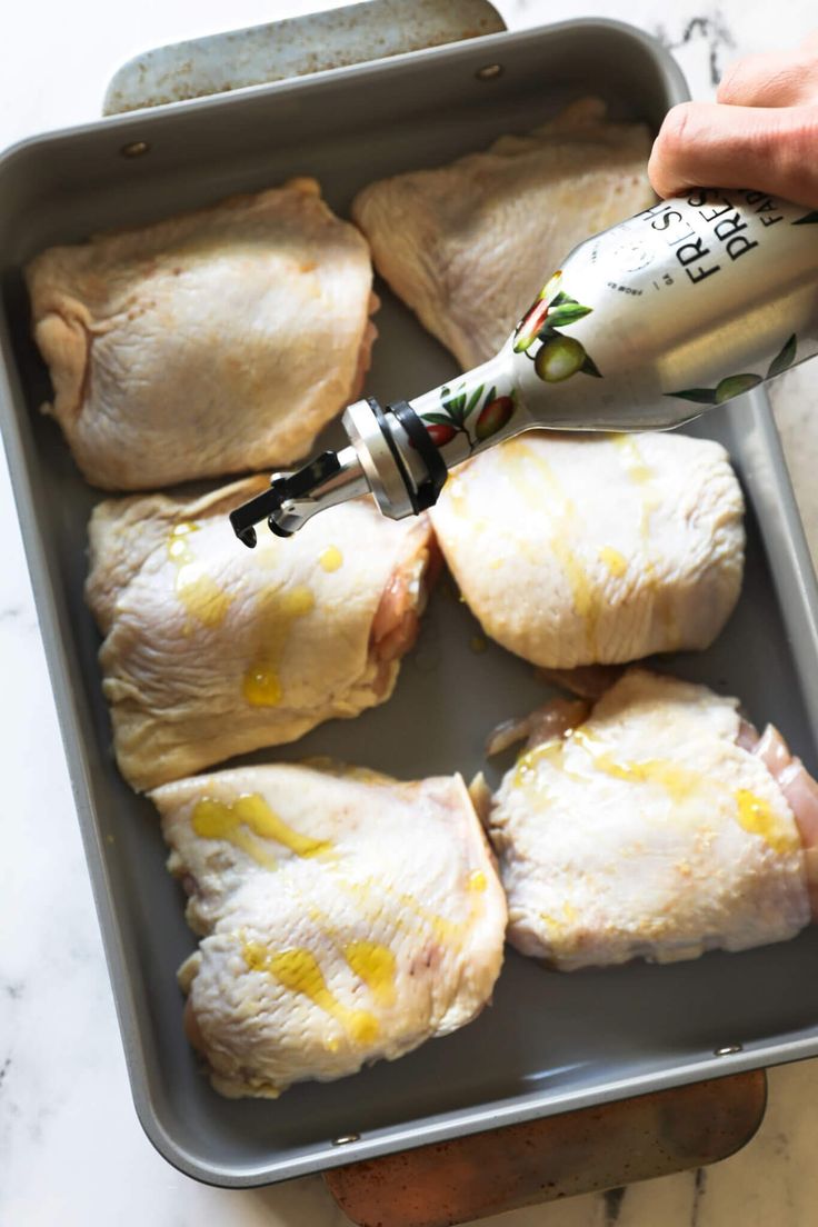 someone is pouring milk on some chicken in a baking pan with other food items nearby