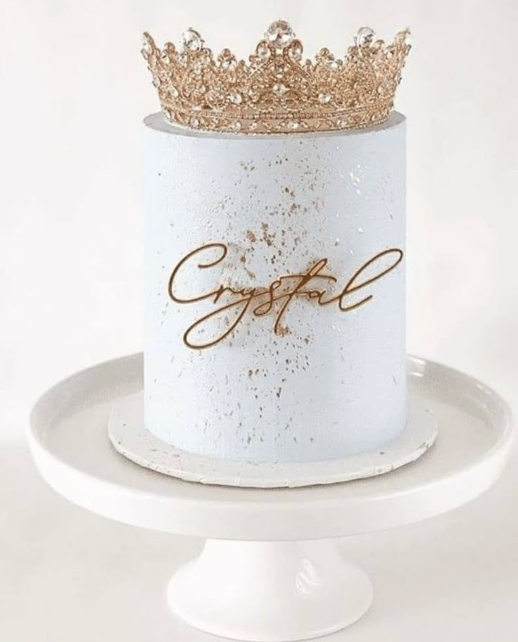 a white cake with gold lettering and a crown on top is sitting on a plate