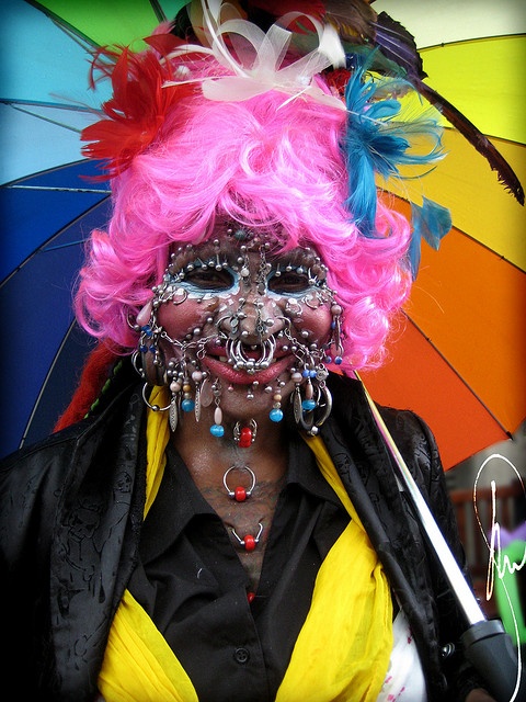 a woman with bright pink hair and face paint holding an umbrella in front of her