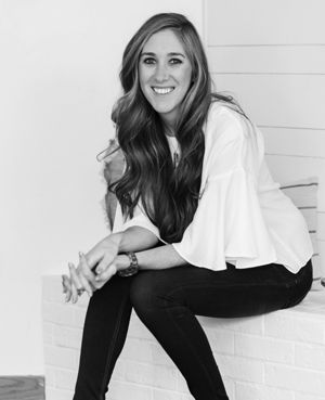 a black and white photo of a woman leaning on a wall with her legs crossed