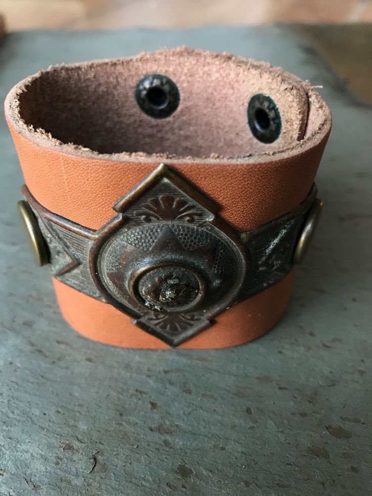 This genuine leather cuff bracelet has a salvaged, brass drawer pull ca. 1900 that is riveted through the cuff using large brass rivets.  It comes with two brass snap locations to allow for sizing adjustments.  The leather on this bracelet has a light tan finish. Item:  A Vintage Sarabeth jewelry is made from authentic antique salvage.  Our inventory consists of glass and crystal prisms, key escutcheons, drawer pulls, and other unique hardware and authentic foreign coins.  Each piece of salvage or coin is hand selected for it's unique characteristics...then built into a one of a kind necklace, bracelet, or key chain.  Our goal is to provide each of our customers with an opportunity to own a curated piece of handmade jewelry at a fair price.  While the salvaged items are the star of the sho Leather Concho Cuff Bracelet, Leather Cuff Bracelet With Concho, Vintage Hand-tooled Leather Cuff Bracelet, Vintage Concho Leather Bracelet For Festival, Vintage Leather Concho Bracelet For Festival, Vintage Leather Festival Bracelets, Vintage Adjustable Leather Bracelet With Concho, Rustic Leather Concho Bracelets, Vintage Brown Adjustable Leather Bracelet