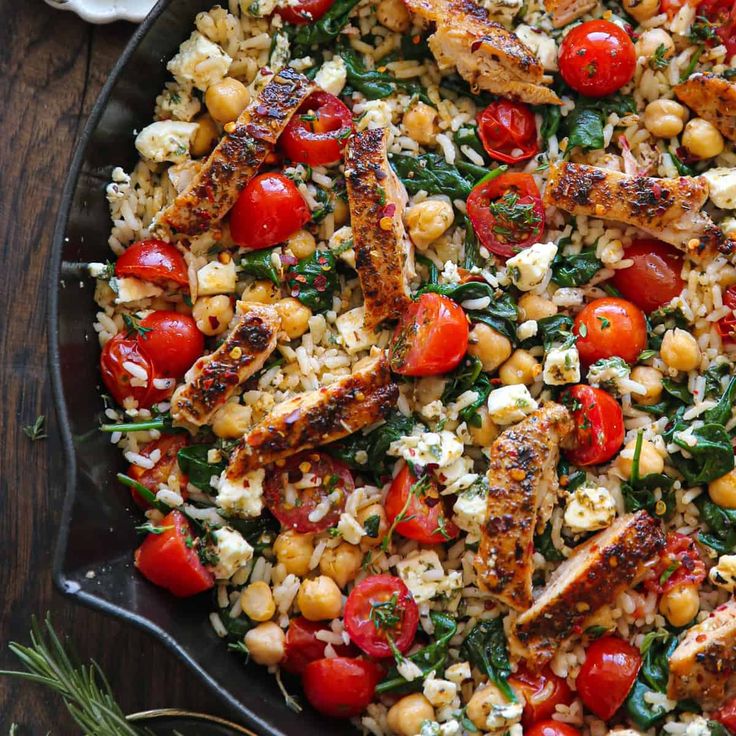 a pan filled with chicken, tomatoes and chickpeas on top of rice covered in herbs