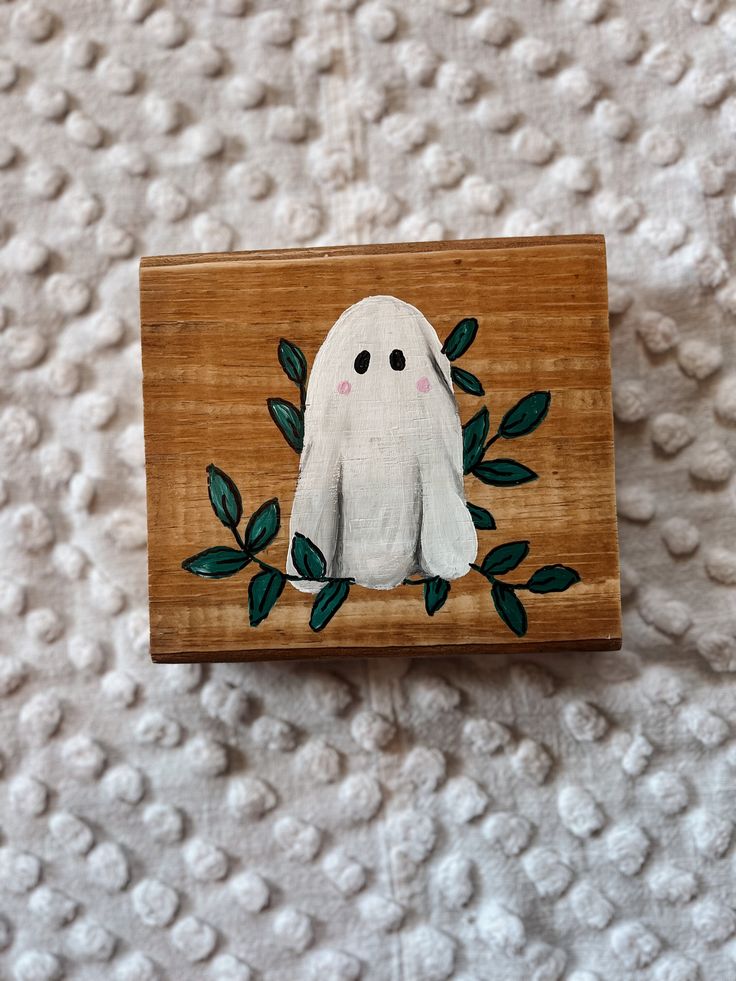 a wooden box with a ghost painted on the side and leaves in front of it