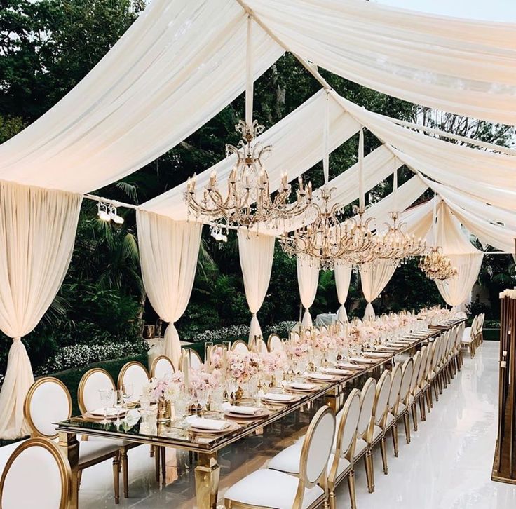 a long table with white chairs and chandeliers