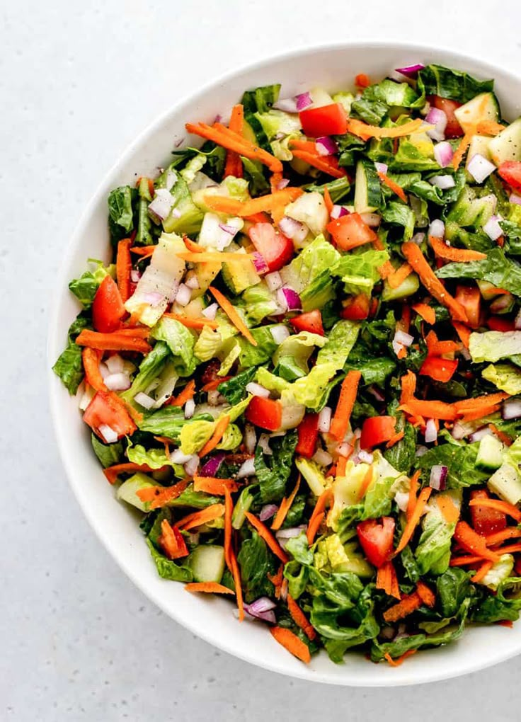 a salad in a white bowl with carrots, celery, onions and lettuce