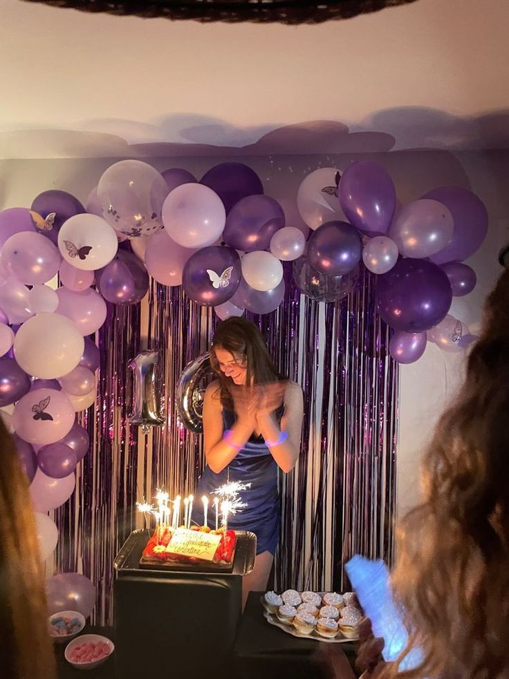 a woman standing in front of a cake with lit candles on it and balloons behind her