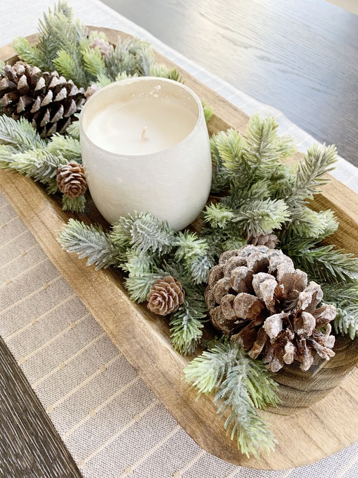 a wooden tray topped with pine cones and a white candle