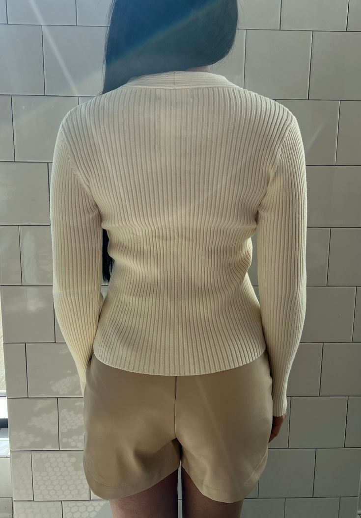 Your classic ribbed knit sweater with a twist. This beautiful off-white garment is cozy and stylish. The unique twist front detail adds a fashionable element to a timeless sweater, making it trendy and comfortable. It is a versatile choice for various occasions, from casual outings to dressier events. Fabric content: 50% rayon, 25% polyester, 22% nylon Washing instructions: dry clean only Imported Model: 5'3" wearing size extra small. Chic Cream Sweater, Cream Ribbed V-neck Knit Top, Elegant White Ribbed Sweater, Chic Ribbed Sweater For Work, Chic Cream Cable Knit Sweater, Chic White Ribbed Knit Top, Chic White Sweater With Ribbed Neckline, Elegant White Sweater With Ribbed Neckline, Versatile Ribbed Sweater For Work