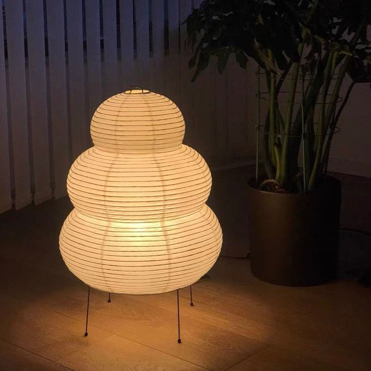 a white lamp sitting on top of a wooden floor next to a potted plant