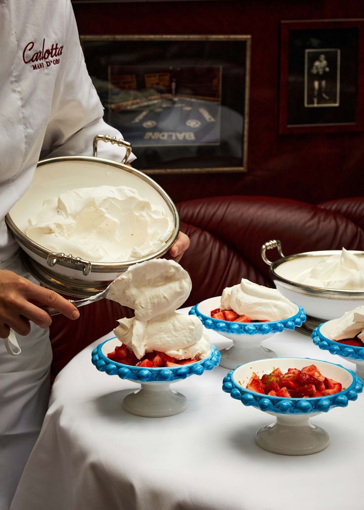 a chef holding a platter full of desserts on top of a white table