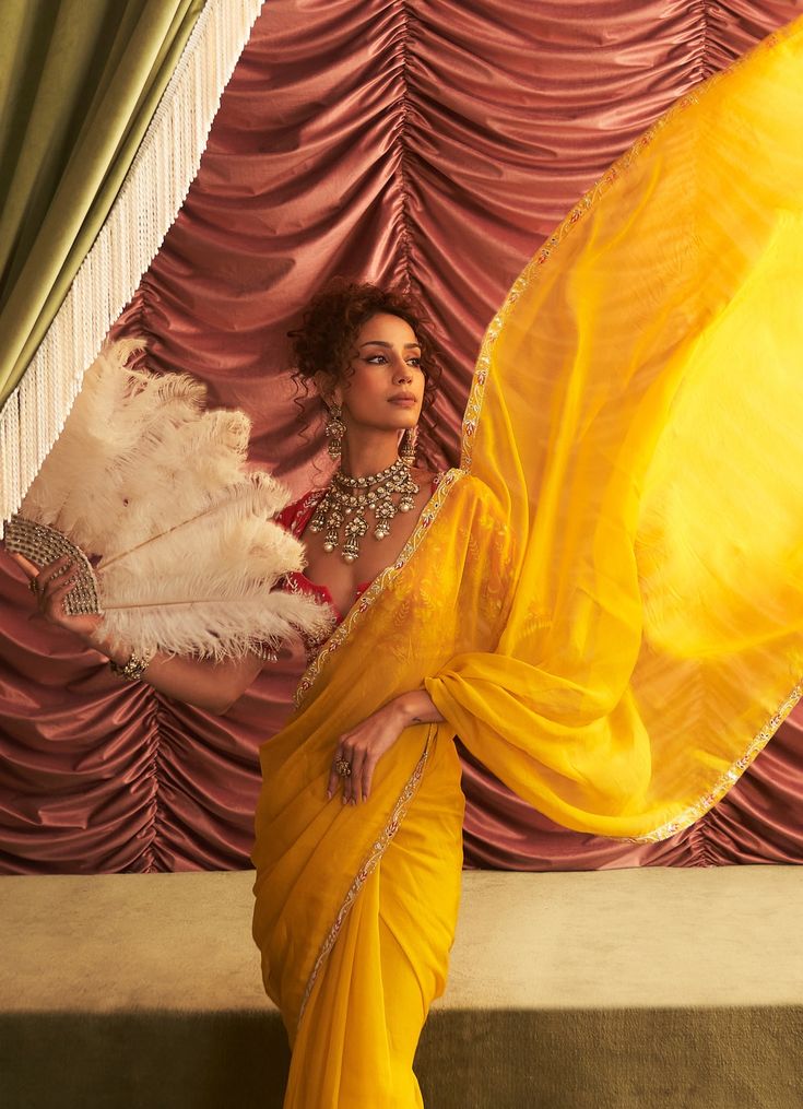 Wrap yourself in the sunshine hues of this stunning Yellow Organza Saree, perfect for making a statement at any festive event. The lightweight organza fabric drapes effortlessly, allowing you to move with grace while ensuring you’re the center of attention at any celebration. Paired with a beautifully embroidered red blouse, this saree is a showstopper for mehendi, sangeet, haldi ceremonies, or any wedding guest looking to add vibrant elegance to their look. Composition : Saree & Blouse - Georgette, Organza, Petticoat - Satin Lycra & Lining - Satin Care: Dry Clean Only and Vacuum Storage This product can be customized for sleeves, blouse length and neckline Delivery : 4-6 weeks as the product is hand crafted. Check Size Guide or choose MySize for free customisation (All Sizes above XL can Organza Blouse With Cutdana For Reception, Diwali Organza Blouse With Traditional Drape, Traditional Drape Organza Blouse With Cutdana, Diwali Blouse In Organza With Traditional Drape, Traditional Drape Organza Blouse For Diwali, Navratri Organza Blouse With Dupatta, Festive Organza Saree Blouse, Organza Blouse Piece For Diwali Reception, Organza Blouse Piece For Reception And Diwali