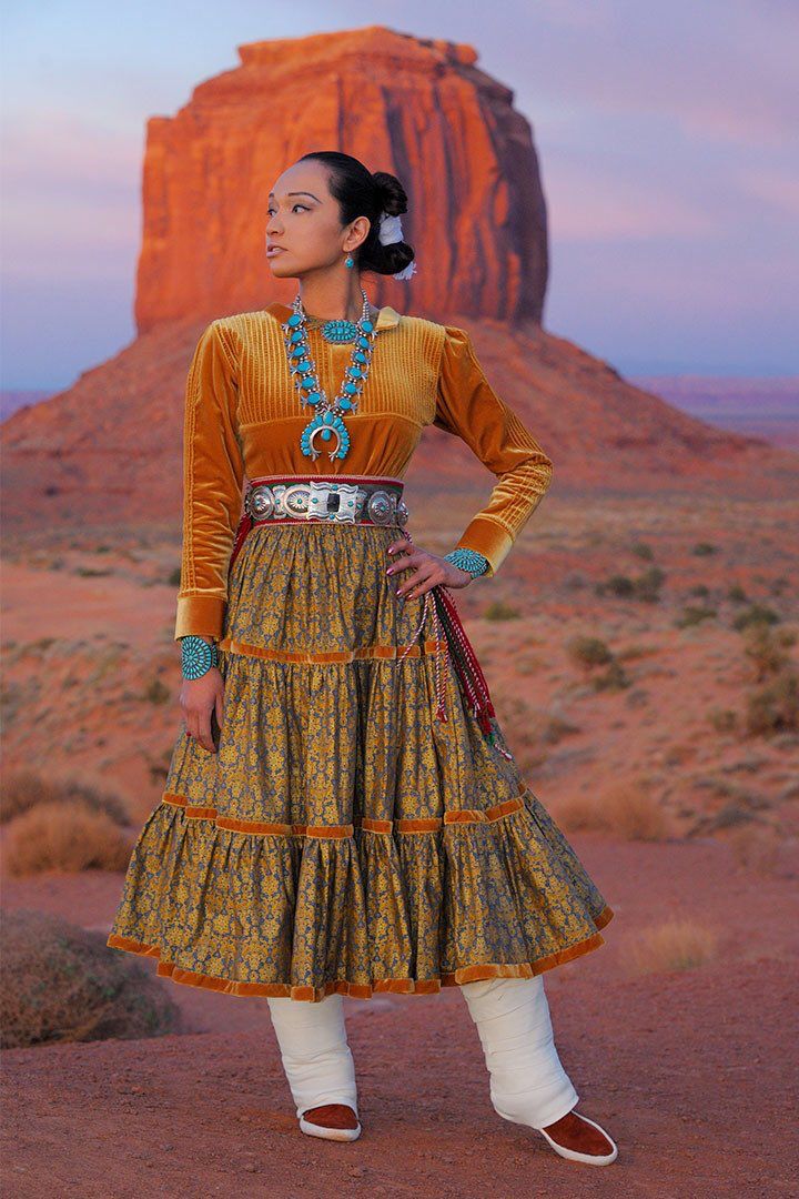 a woman standing in front of a large rock formation with a desert landscape behind her