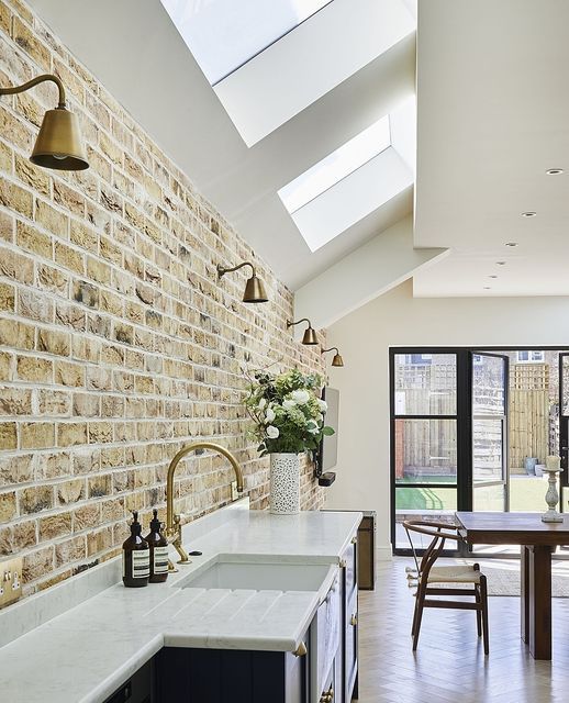 a kitchen with an exposed brick wall and white counter tops, along with wooden chairs