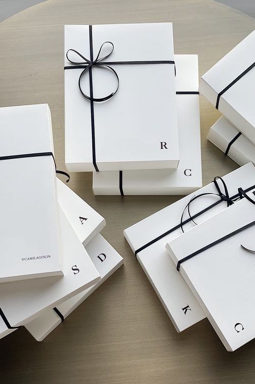 four white gift boxes tied with black ribbon on top of each other, sitting on a table