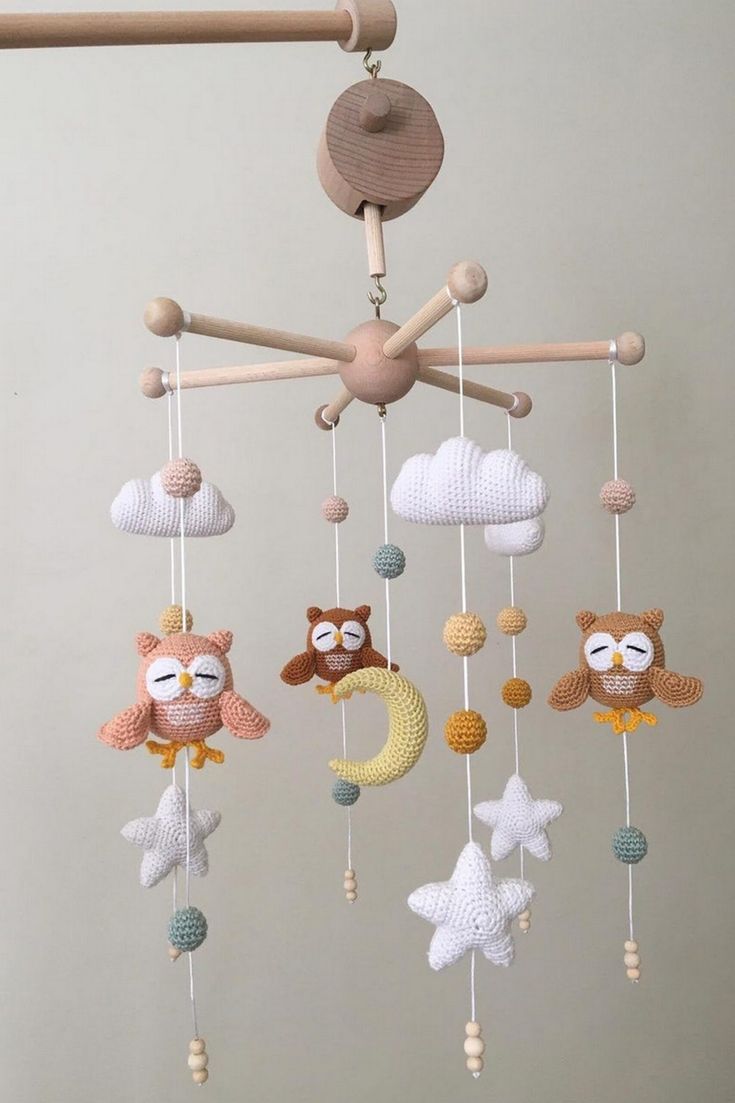 a crocheted mobile with owls, stars and clouds hanging from the ceiling in front of a gray wall