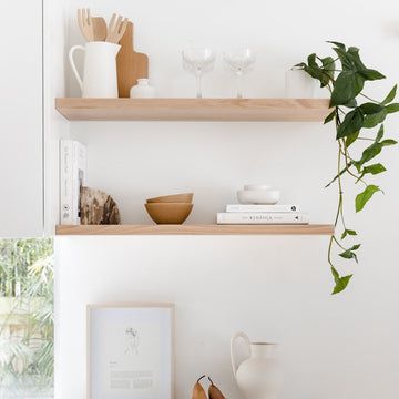 two wooden shelves filled with dishes and vases on top of each other next to a potted plant