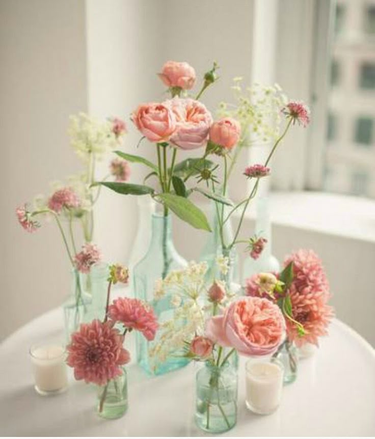 an image of flowers in glass vases on a white table with candles and windows