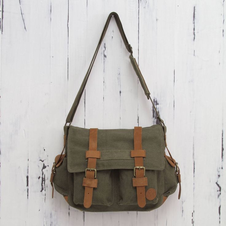 Crafted of sturdy green canvas this roomy messenger bag keeps things organized. Four outer pockets are easily accessible while a zipper pocket is hidden on the inside of the flap. By Karina and Maybee the bag is lined in dark beige cotton and opens to reveal another zipper pocket. Leather trim adds to its appeal and the shoulder strap is adjustable in length. Green Canvas Satchel For School, Green Shoulder Satchel With Pockets, Green Bags With Multiple Pockets For Everyday Use, Khaki Satchel With Pockets For School, Khaki Canvas Shoulder Bag With Multiple Pockets, Green Canvas Bag With Adjustable Strap, Green Everyday Bag With Multiple Pockets, Green Everyday Bags With Multiple Pockets, School Satchel With Pockets In Khaki