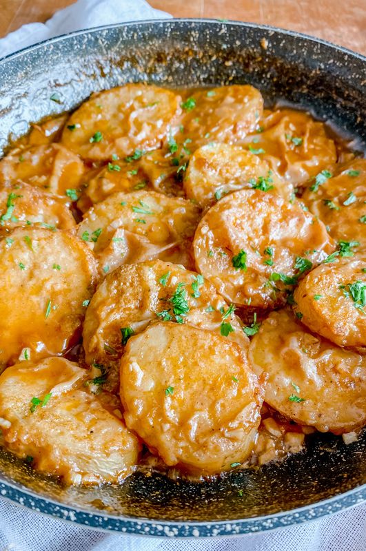 a pan filled with potatoes covered in gravy and garnished with parsley