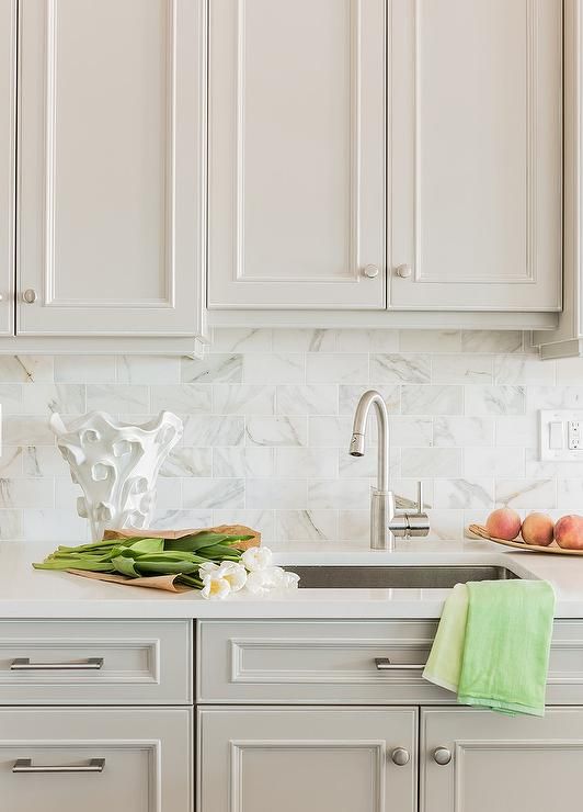 a kitchen with white cabinets and marble counter tops, along with green towels on the sink