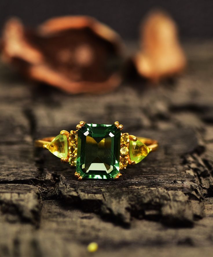 an emerald ring sitting on top of a piece of wood next to nuts and shells