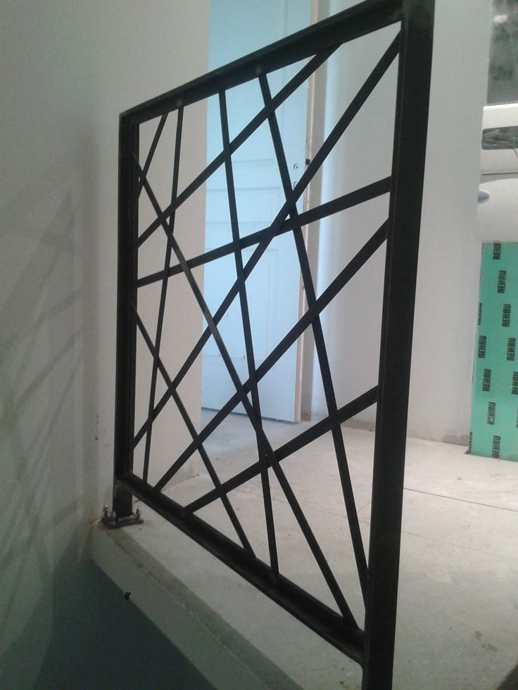 an open window in the corner of a room with white walls and black metal bars