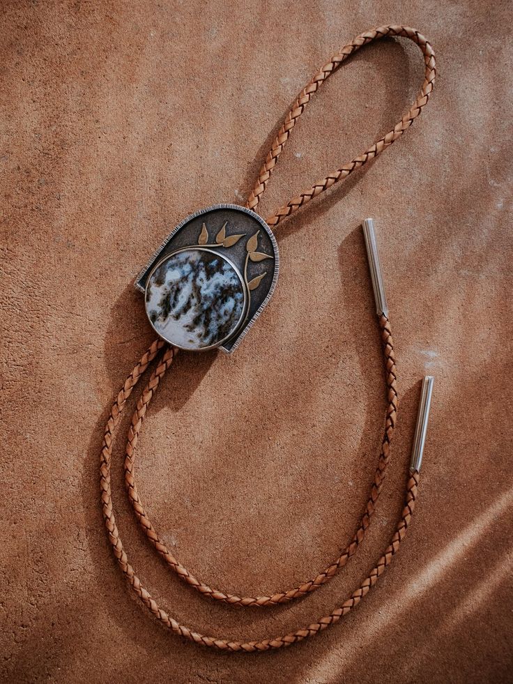 Bolo tie featuring Graveyard Plume Agate, sterling silver, brass, and braided leather cord. Modern Bolo Tie, Medieval Cowboy, Plume Agate, Gold Teeth, Bolo Ties, Brown Wedding, Bolo Tie, Pattern Play, To Be Loved