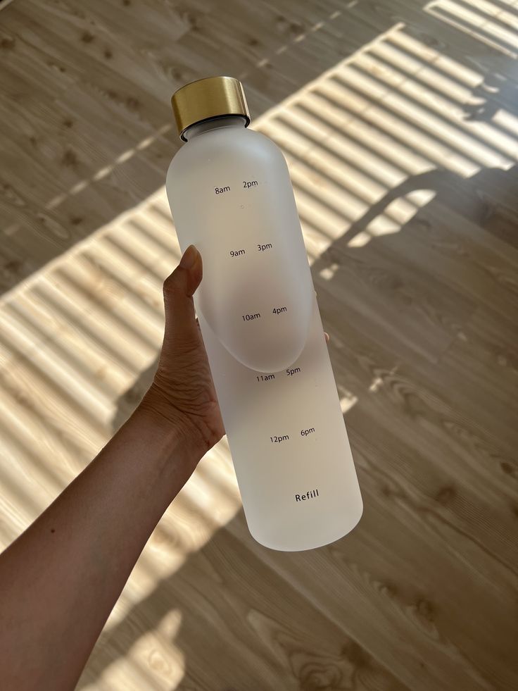 a hand holding a white water bottle on top of a wooden floor