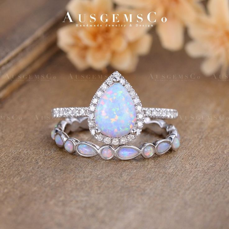 a white opal and diamond ring set on top of a wooden table with flowers in the background