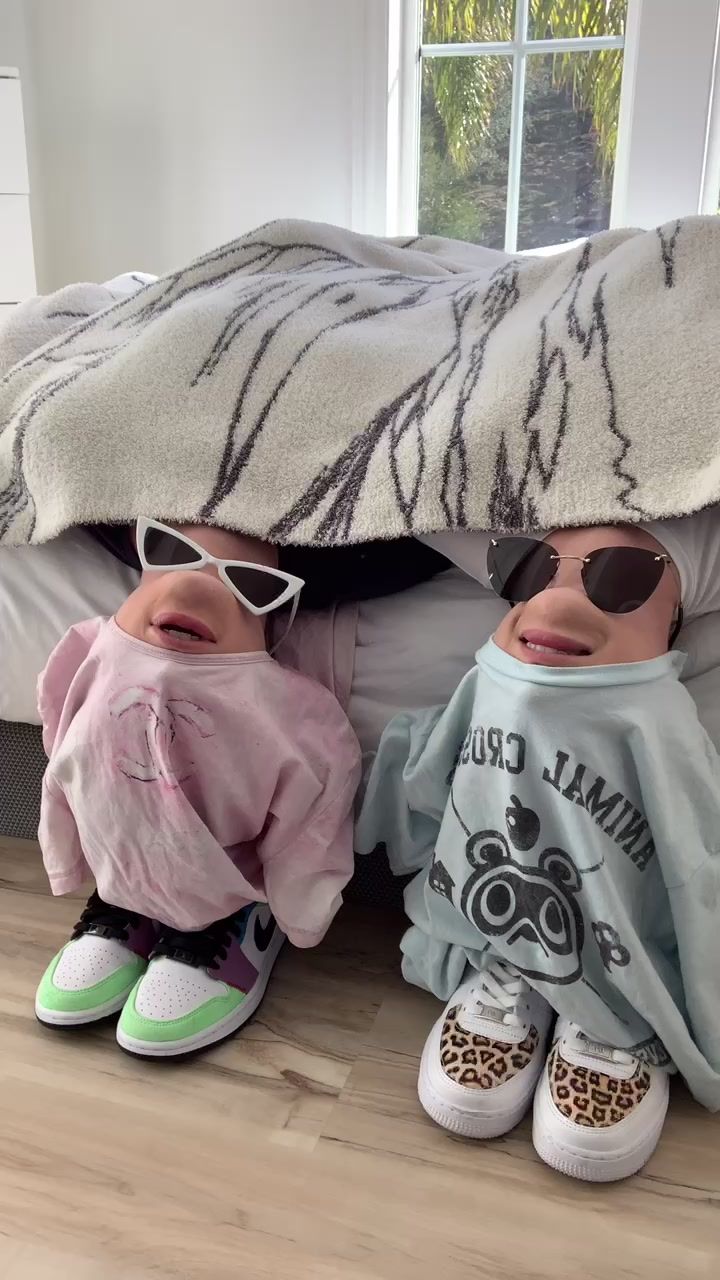 two dolls sitting under a blanket on the floor