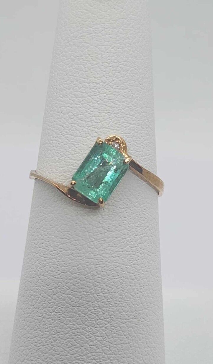 a ring with an emerald colored stone in it on a white napkin holder and gold plated metal band