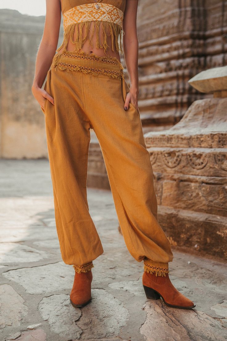 a woman standing in front of a stone wall wearing brown pants and a crop top